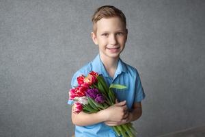 une mignonne garçon dans une chemise détient une coloré bouquet de tulipes dans le sien mains. espace pour texte photo