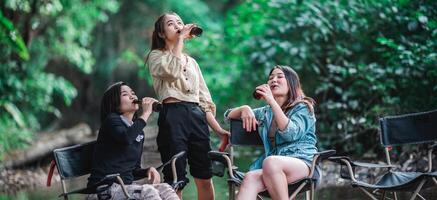 jeunes femmes assises et buvant des boissons en camping en forêt photo