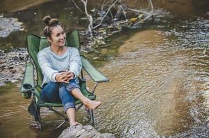 jeune femme assise sur une chaise de camping en ruisseau pour se détendre photo