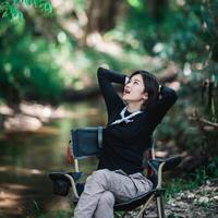 heureuse jeune femme assise sur une chaise en camping en forêt photo