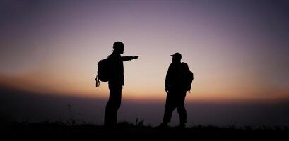 silhouette de promeneur Hommes avec sac à dos rester sur falaise et pense sur le Haut Montagne à le coucher du soleil photo