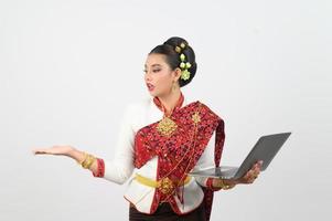 portrait de magnifique thaïlandais femme dans traditionnel Vêtements posant avec portable ordinateur photo