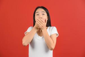 portrait de excité Jeune asiatique femme dans blanc T-shirt mains couverture bouche isolé sur rouge Contexte photo