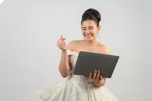 Jeune belle mariée asiatique pose avec un ordinateur portable à la main photo