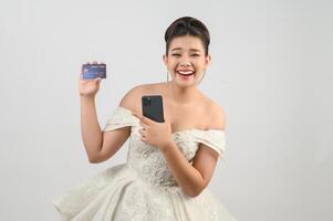 Jeune asiatique magnifique la mariée affectation avec crédit carte et téléphone intelligent dans main photo