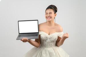 Jeune belle mariée asiatique pose avec un ordinateur portable maquette à la main photo