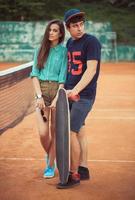 Jeune couple permanent sur une planche à roulette sur le tennis tribunal photo