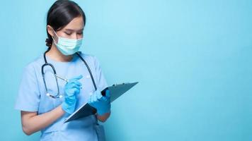Médecin portant un masque facial et un stéthoscope écrit sur un presse-papiers sur fond bleu photo