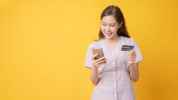 femme asiatique, sourire, tenue, carte crédit, et, regarder téléphone portable, sur, fond jaune photo