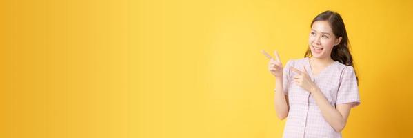 Femme asiatique souriant et faisant des gestes vers l'espace de copie sur fond jaune