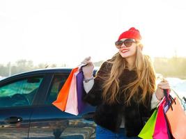 souriant caucasien femme en portant sa achats sac près le voiture photo