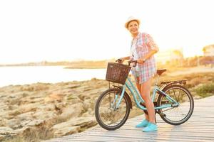 insouciant jolie femme avec vélo équitation sur une en bois chemin à le mer photo