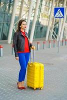 femme dans brillant vêtements avec le Jaune valise est permanent près le aéroport photo