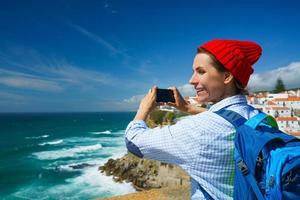 femme avec une sac à dos fait du une photo sur le téléphone intelligent de une magnifique panorama de le océan côte près azenhas faire mar, portugal