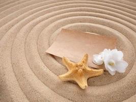 lettre dans le sable. artisanat papier avec blanc fleur et étoile de mer sur le le sable dans le forme de spirale. concept tranquille Zen photo