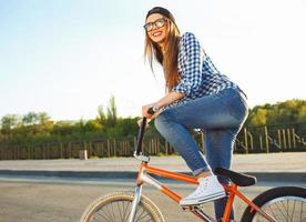 charmant Jeune femme dans une chapeau équitation une vélo sur ville Contexte dans le lumière du soleil Extérieur photo