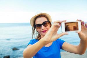 fille dans le chapeau fabrication selfie par le téléphone intelligent sur le Contexte de mer côte, adriatique mer photo