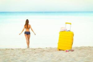 Jaune valise sur le plage et une fille des promenades dans le mer dans e photo