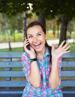 portrait de une Jeune femme dans une parc parlant sur le téléphone photo