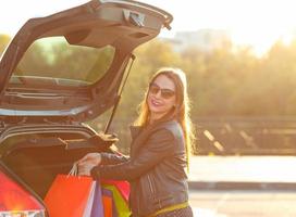 souriant caucasien femme en mettant sa achats Sacs dans le voiture tronc photo