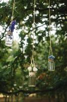 mariage décorations de petit bouteilles rempli avec des roses et autre fleurs suspendu sur une fil entre des arbres dans le les bois photo