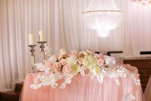 décoration de table de mariage festive avec lustres en cristal, chandeliers dorés, bougies et fleurs roses blanches. jour de mariage élégant. photo