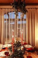 de fête table réglage pour fête Noël et Nouveau année vacances dans vivant chambre. à manger table avec traditionnel dîner repas décoré brûlant bougies, sapin branches, Noël boules, vacances guirlandes photo