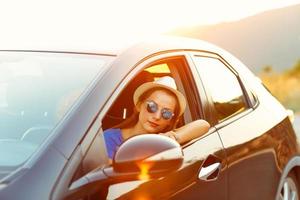souriant femme conduite une voiture à le coucher du soleil photo