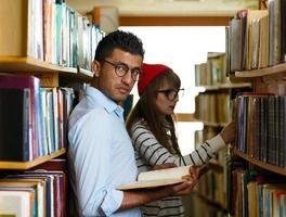 Jeune étudiant couple choisir livres dans le bibliothèque photo