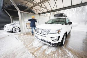 homme lavant une voiture suv américaine à eau haute pression avec galerie de toit au lavage en libre-service par temps froid. photo