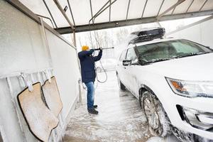homme lavant une voiture suv américaine à eau haute pression avec galerie de toit au lavage en libre-service par temps froid. photo