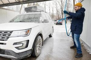 homme lavant une voiture suv américaine avec galerie de toit lors d'un lavage en libre-service par temps froid. photo