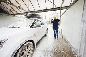 homme lavant une voiture suv américaine à eau haute pression avec galerie de toit au lavage en libre-service par temps froid. photo