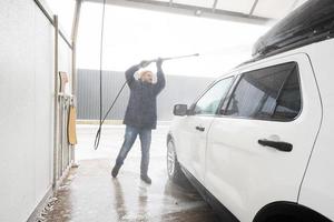 homme lavant une voiture suv américaine à eau haute pression avec galerie de toit au lavage en libre-service par temps froid. photo