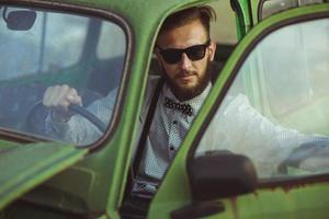 Jeune élégant Beau homme, portant chemise et des lunettes de soleil, conduite vieux voiture photo