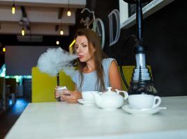magnifique femme fumeur une narguilé et en utilisant téléphone intelligent dans une café photo