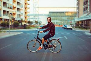 élégant homme dans des lunettes de soleil équitation une bicyclette sur ville rue photo