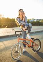 charmant Jeune femme dans une chapeau équitation une vélo sur ville Contexte dans le lumière du soleil Extérieur photo
