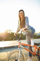 charmant Jeune femme dans une chapeau équitation une vélo sur ville Contexte dans le lumière du soleil Extérieur photo