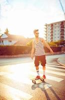 homme dans des lunettes de soleil avec une planche à roulette sur une rue dans le ville à le coucher du soleil lumière photo