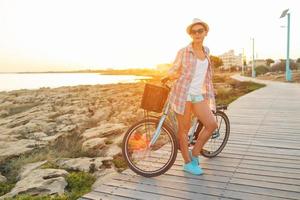 insouciant femme avec vélo équitation sur une en bois chemin à le mer, ayant amusement et souriant photo