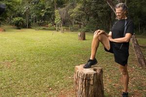 mature homme à l'extérieur à une local parc Faire élongation le sien jambe avant travail en dehors photo