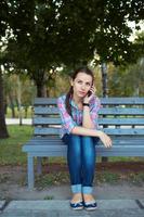 portrait de une femme dans une parc sur une banc parlant sur le téléphone photo