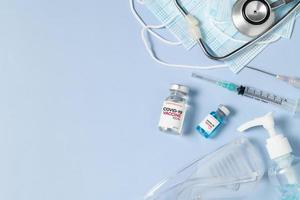 une Fiole de le convoitise 19 vaccin avec seringue et stéthoscope sur une chirurgical masque sur bleu arrière-plan, photo