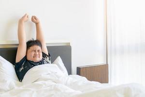 obèse garçon réveiller en haut et étendue bras sur lit dans Matin. paresseux et du repos photo