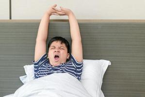 obèse graisse garçon se réveille en haut et élongation sur lit dans matin, santé se soucier et bien Matin photo