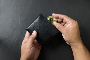 homme d'affaire en mettant bitcoin dans une noir cuir portefeuille sur noir Contexte. économie bitcoin photo