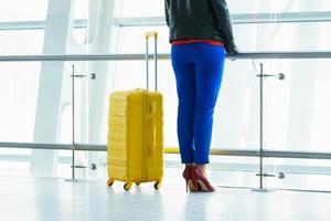 femme dans brillant vêtements avec Jaune valise des stands dans le aéroport