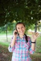 portrait de une souriant femme dans une parc parlant sur le téléphone photo