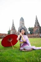magnifique thaïlandais fille dans traditionnel robe costume rouge parapluie comme thaïlandais temple où est le Publique lieu, thaïlandais femme dans traditionnel costume de Thaïlande. photo